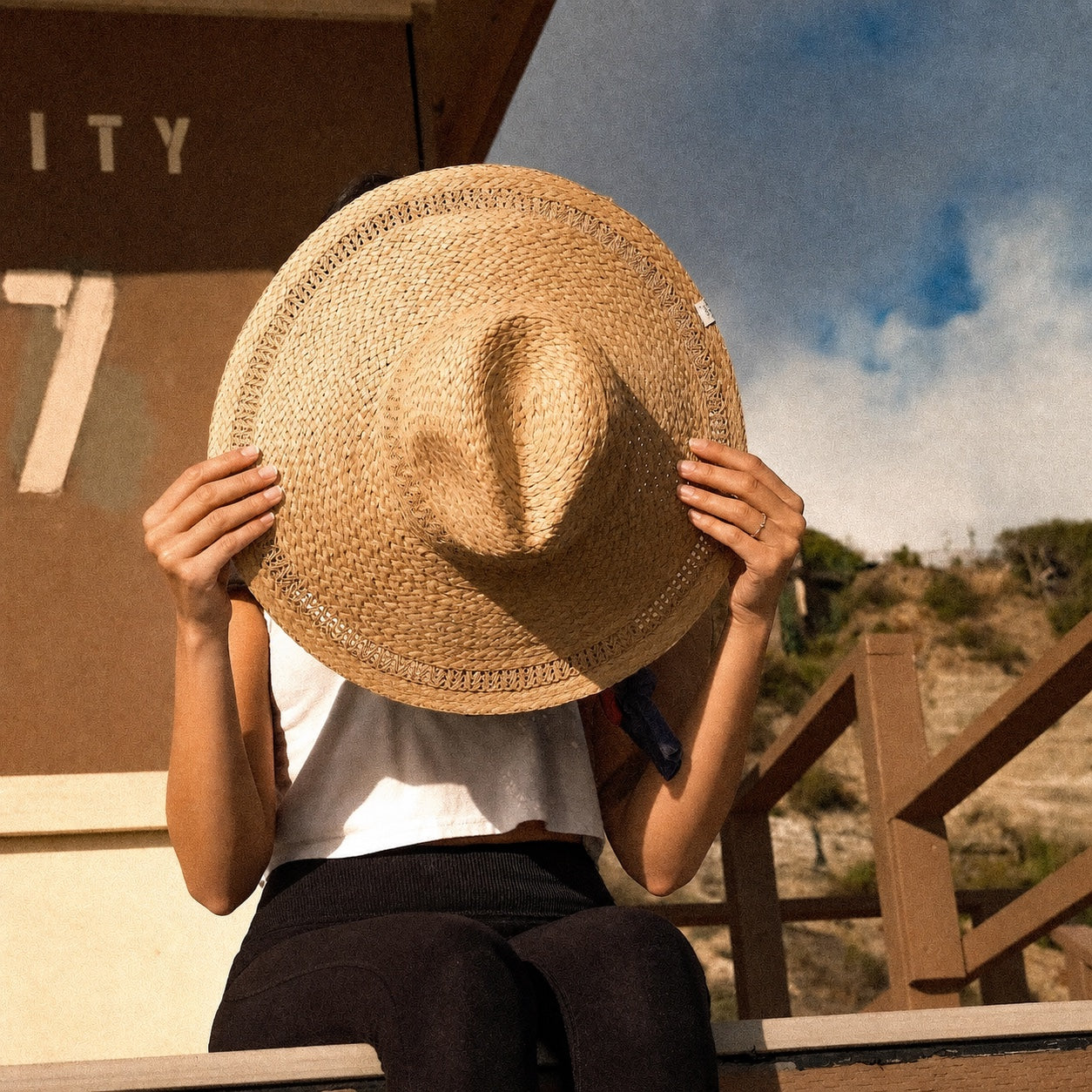 Young woman holding a woven Nami Sun Hat at the beach